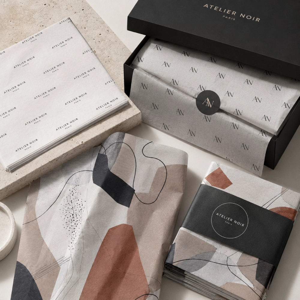 Image of Custom printed tissue paper featuring repeating logos, short brand text, and modern abstract artwork arranged with premium black gift packaging.