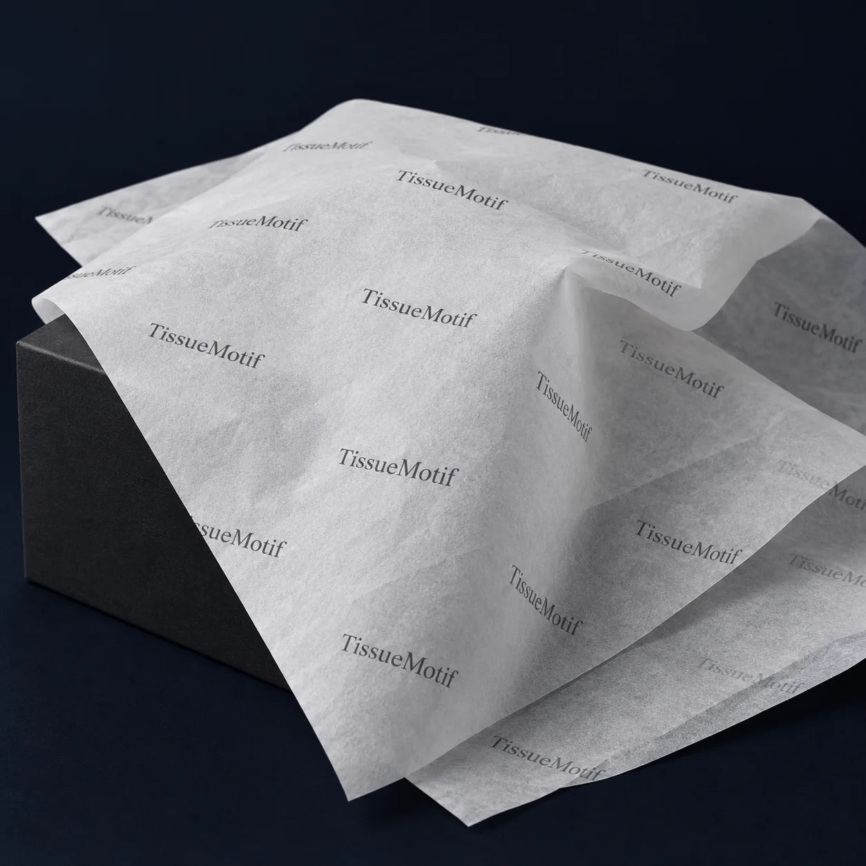 Lightweight natural white printed tissue draped over a charcoal block, showing softly translucent folds