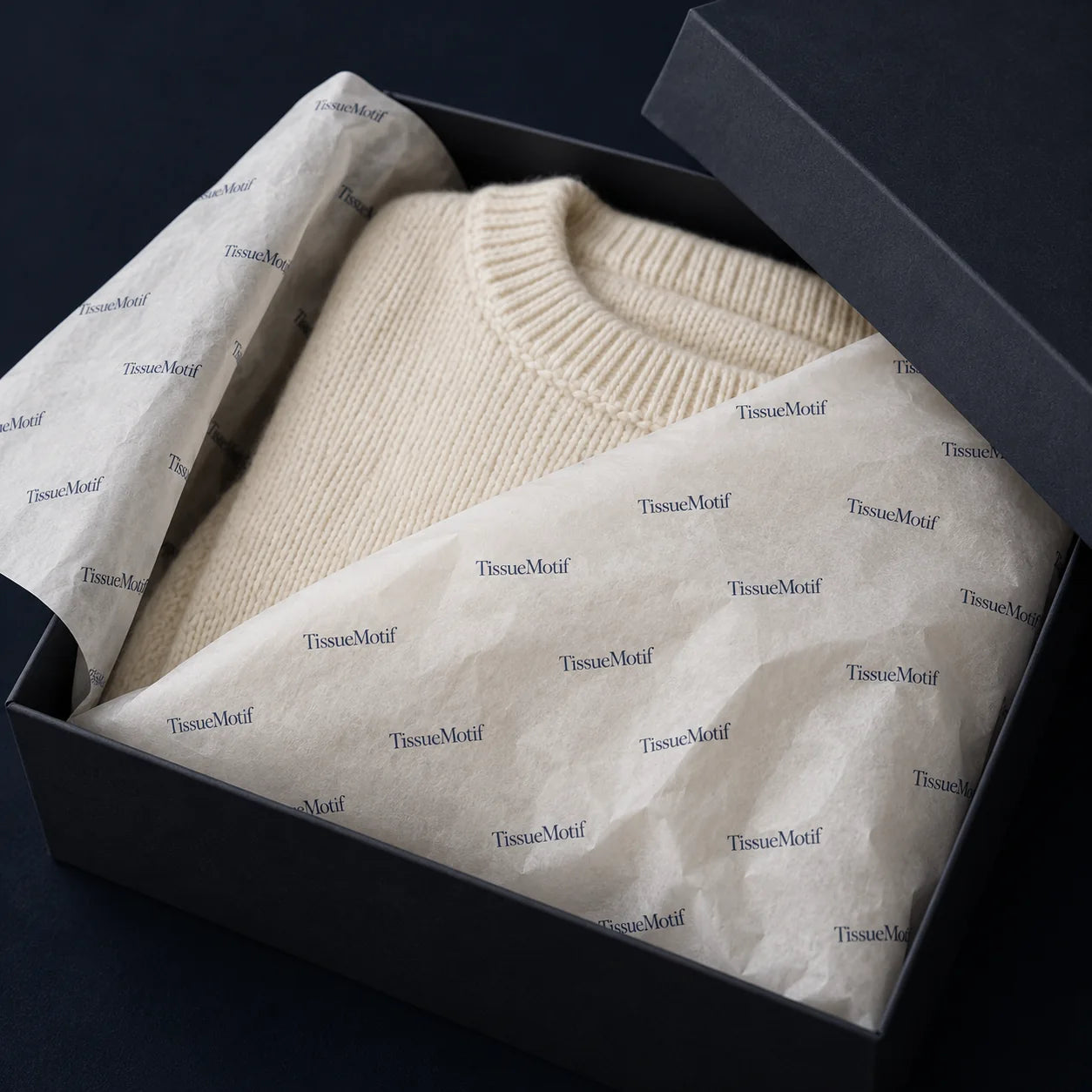 A folded cream knitted garment wrapped in custom printed tissue inside an apparel box